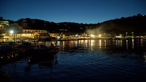 Une zone riveraine avec des bateaux amarrés, des bâtiments illuminés et une colline en arrière-plan.