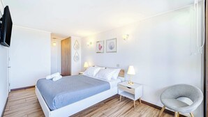 Un dormitorio ordenado con una cama, mesitas de noche, una silla y una obra de arte en la pared.