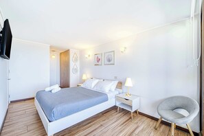 A neatly arranged bedroom with a bed, bedside tables, a chair, and wall-mounted artwork.
