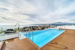 A swimming pool on a deck with a view of the sea and a mountain in the distance.