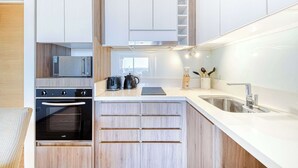 Una cocina moderna con armarios blancos, horno empotrado, microondas y pileta de acero inoxidable.