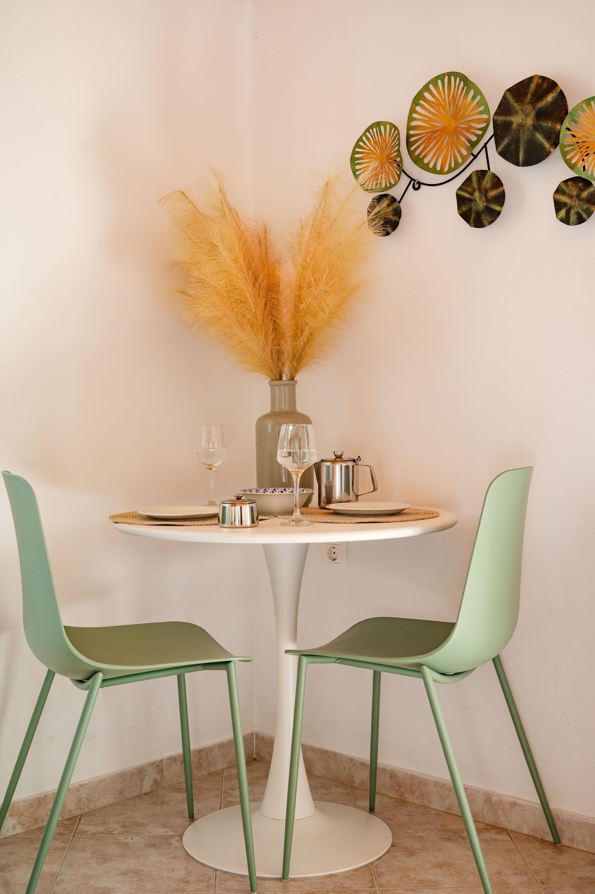 Une table à manger avec deux chaises, un vase contenant des plantes séchées et un élément décoratif mural.