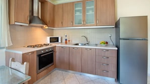 Une cuisine moderne avec des meubles en bois, des appareils en acier inoxydable, une table en verre et un revêtement mural en carreaux.