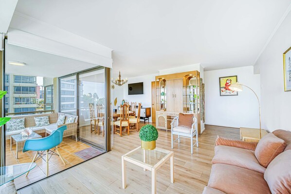 A modern living room with a sofa, a dining table, and chairs. There is a glass coffee table with a plant on it. - Beach Paradise 4BR with view (Viña del Mar)