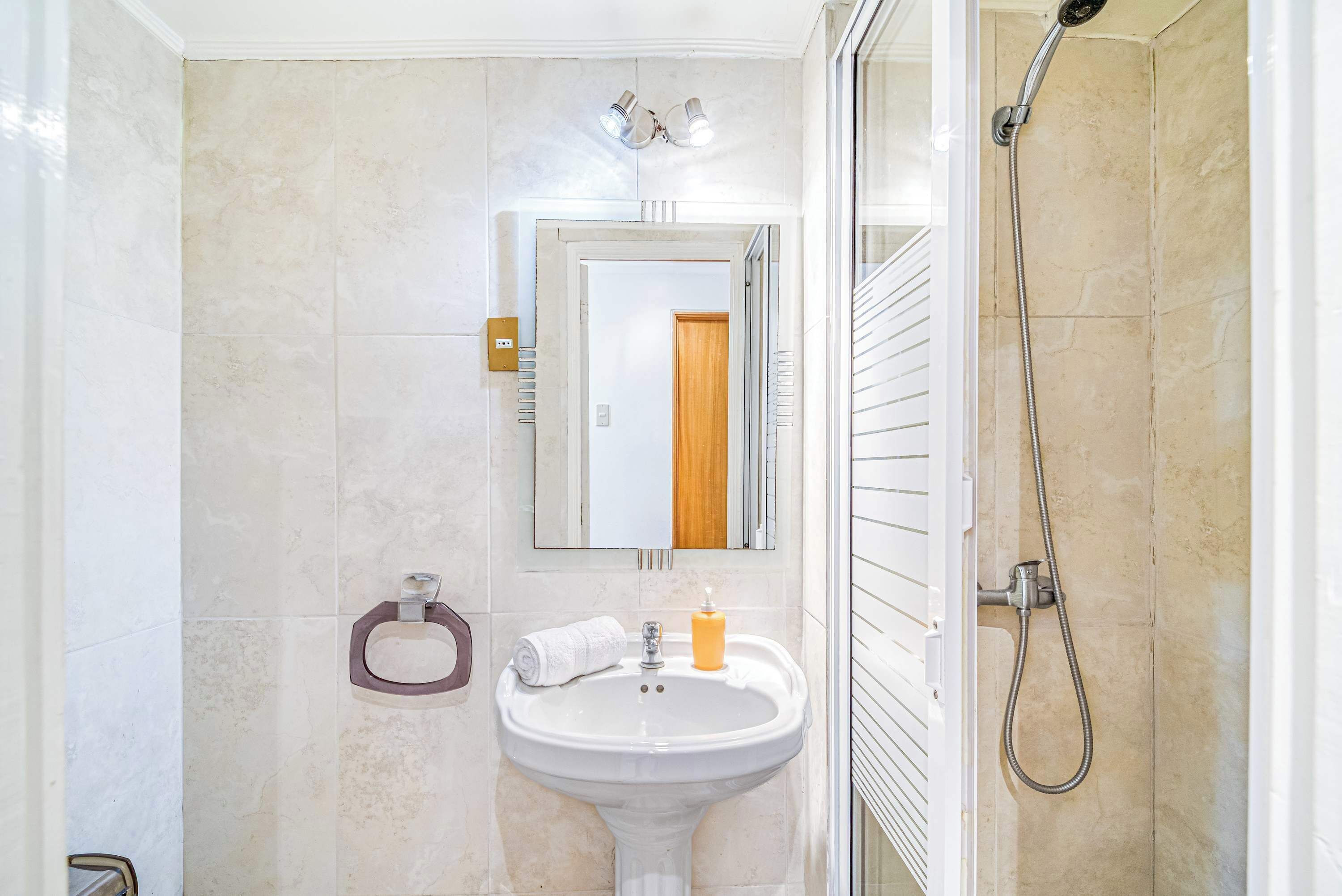 Un baño con lavamanos blanco, un espejo, ducha e inodoro.