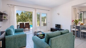 Ein modernes Wohnzimmer mit Türkis-Sofas, einem Couchtisch, einem Fernseher und einem Balkon mit Pool.
