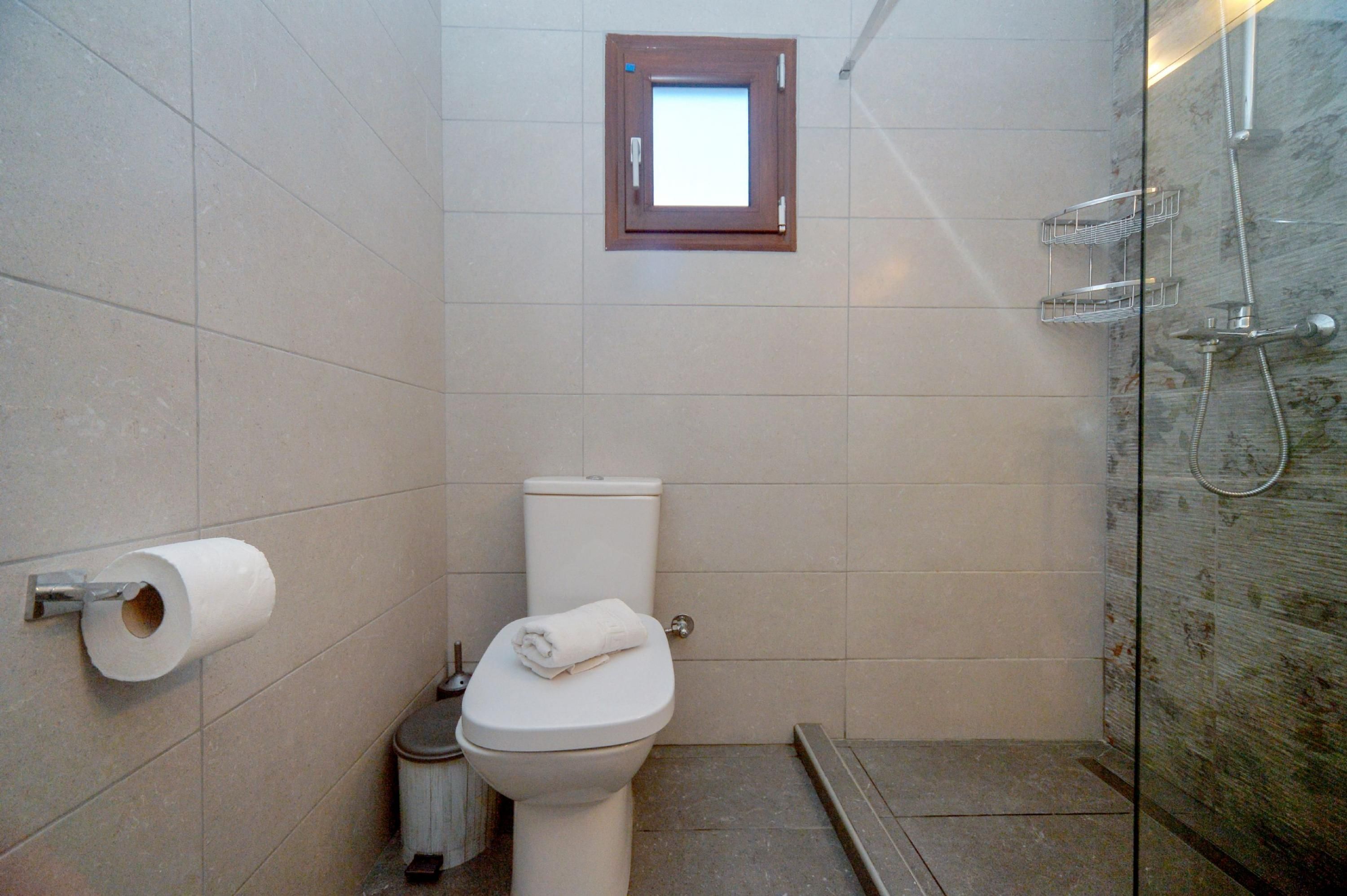 Ein Badezimmer mit Toilette, Toilettenpapier, einem kleinen Fenster und einer Duschkabine.