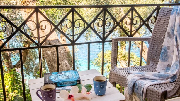 A balcony with a view of the sea, a wicker chair, a table with books and a coffee mug, and a decorative flower. - Aglaia Studio in Longos (Longos)