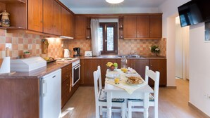 A compact kitchen with wooden cabinets, a built-in dishwasher, and a dining area with a table set for two. - Aglaia Studio in Longos (Longos)