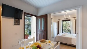 A breakfast table with fruits, a croissant, and orange juice. There is a bed with a white bedspread and a chandelier. - Aglaia Studio in Longos (Longos)