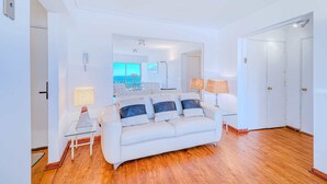 A modern living room with a white sofa, glass coffee table, and lamps. A large mirror reflects the room and a view of the sea. - Beach View 2D increible ubicacion (Valparaíso)