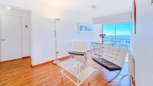 A modern living room with a glass coffee table, a white sofa, a chair, and a view of the ocean. - Beach View 2D increible ubicacion (Valparaíso)