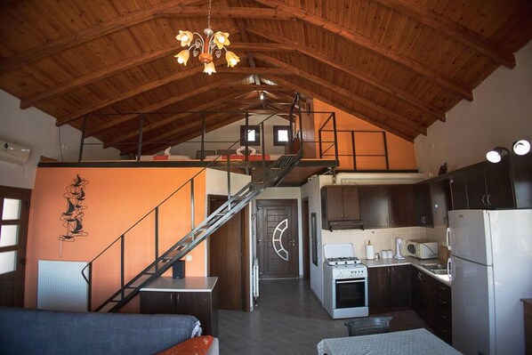 A spacious loft-style room with a high ceiling, a staircase, a kitchenette, and a bed. - Foula House in Magnisia (Magnisia)