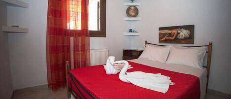 Een slaapkamer met een rood bedlaken, een houten hoofdbord, een wereldbol, een schilderij en een rood gordijn.
