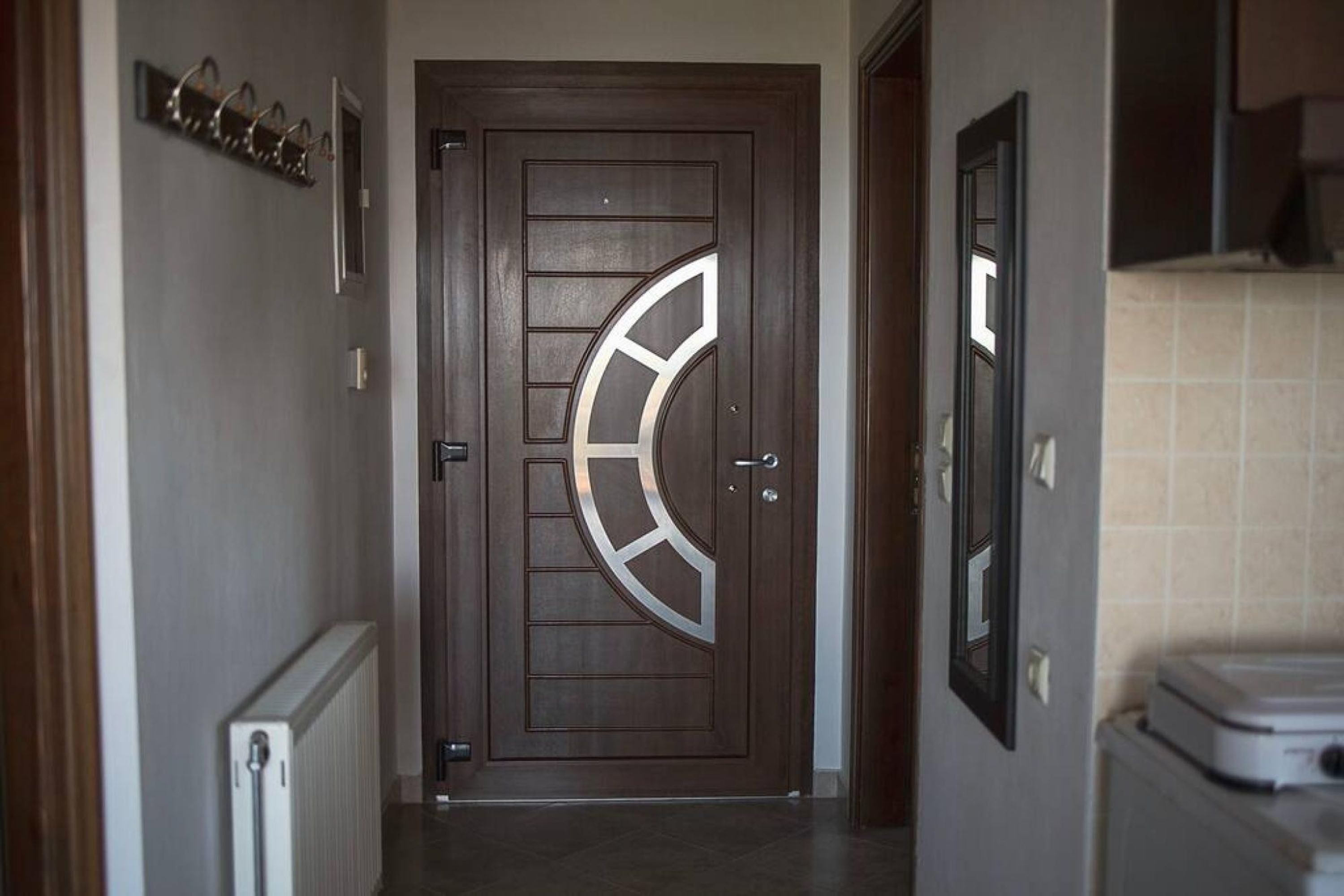 Un pasillo con puerta de madera que presenta un diseño geométrico, un radiador y una pared de azulejos.