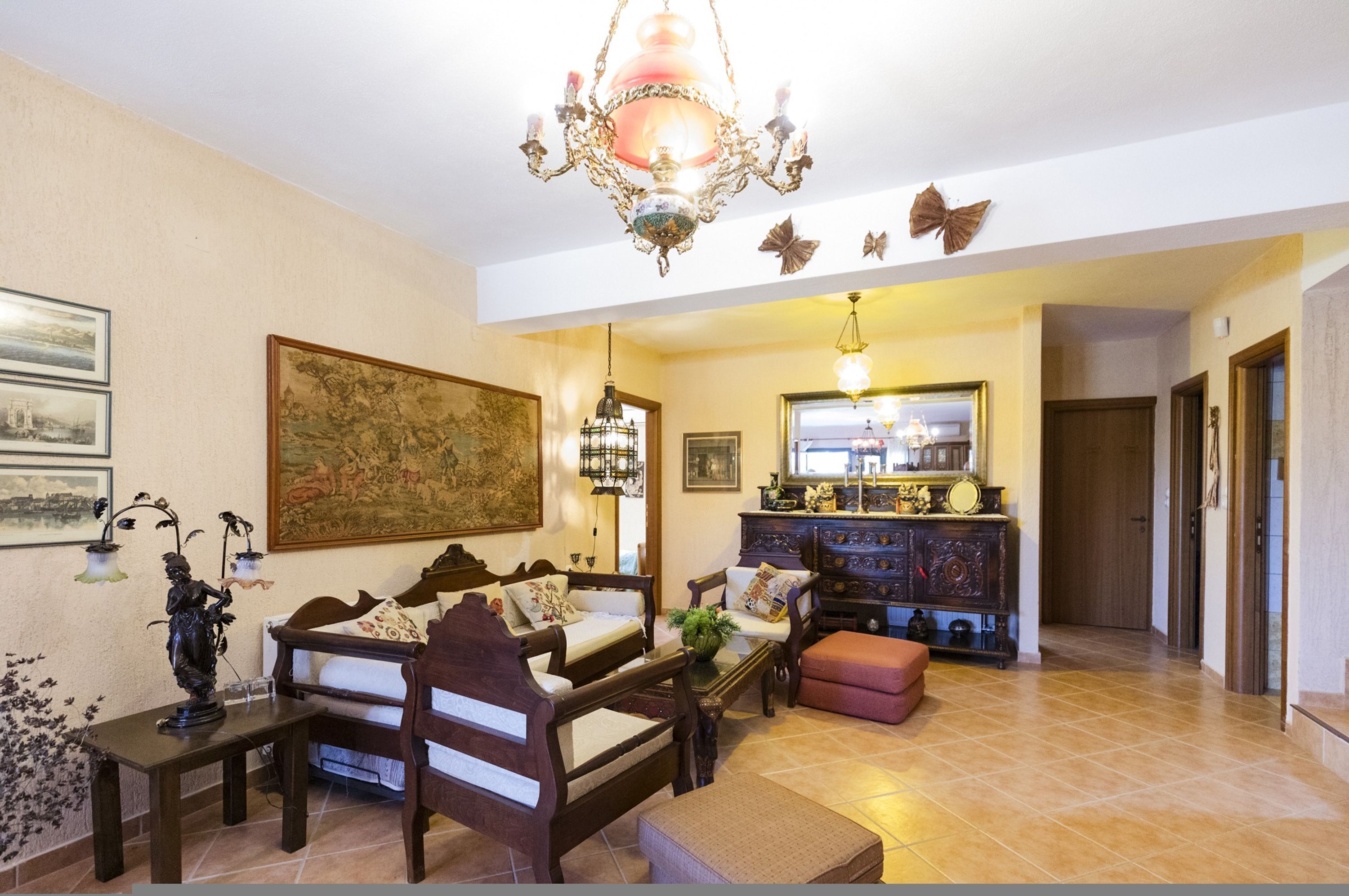 A spacious living room with a large painting, a chandelier, and a wooden cabinet.