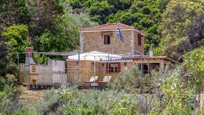 A stone house with a tiled roof, surrounded by greenery and a fenced area with lounge chairs. - Nerissa Cottage - Skopelos Glossa (Glossa)