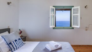 A bedroom with a bed, a window with an open shutter, a nightstand, and a view of the sea. - Nerissa Cottage - Skopelos Glossa (Glossa)