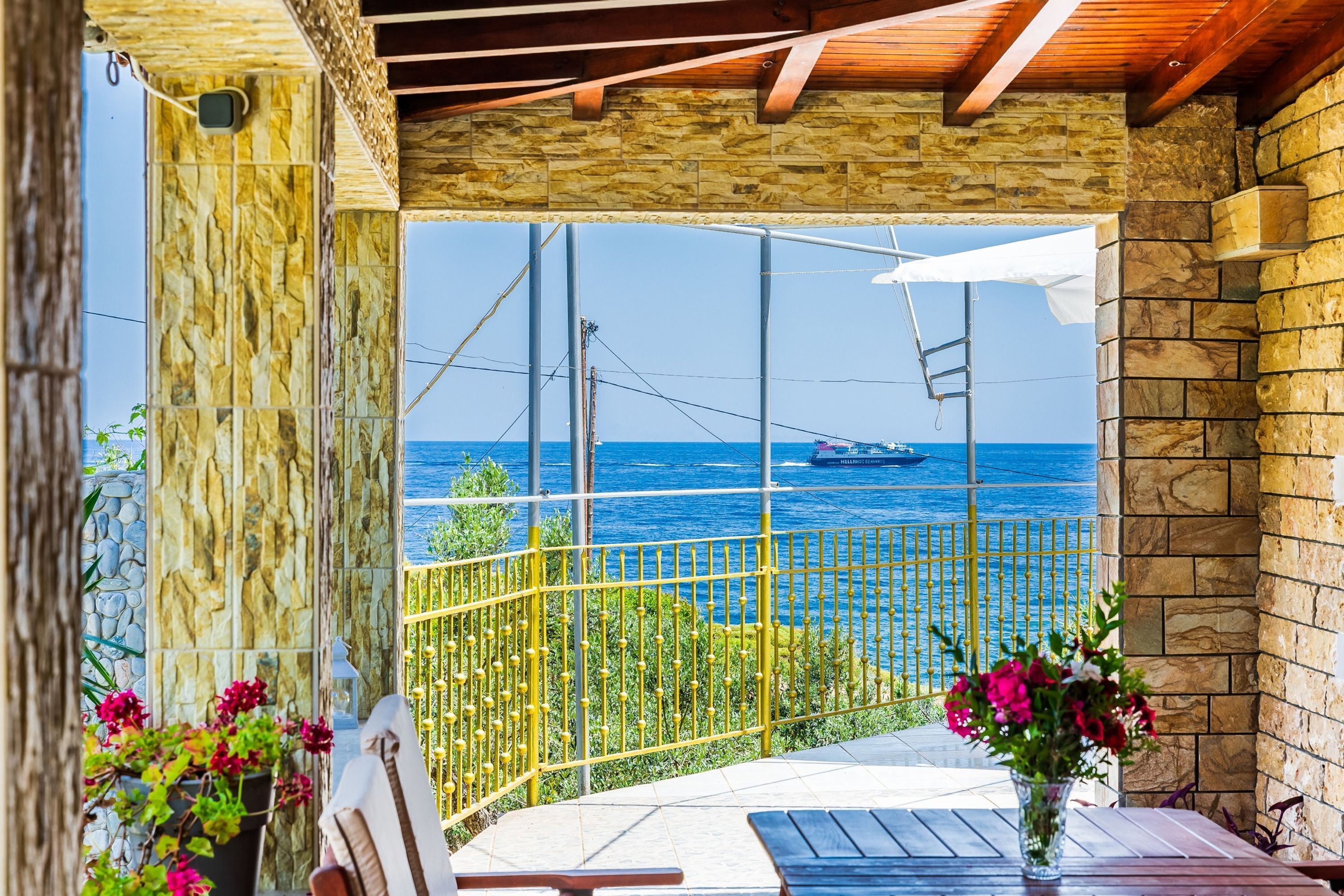 A balcony with a stone wall, a view of the sea, and a ship in the distance.