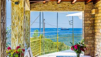 A balcony with a stone wall, a view of the sea, and a ship in the distance.