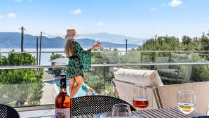 A balcony with a glass railing overlooking a pool and mountains. - Two-Bedroom Apartment Sea View (Nikiana)