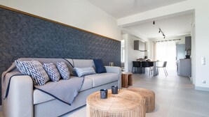 A modern living room with a grey sofa, patterned cushions, and two wicker coffee tables. - Two-Bedroom Apartment Sea View (Nikiana)