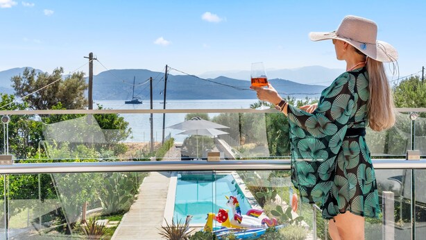 A person standing by a pool with a view of mountains and a body of water. - Two-Bedroom Apartment Sea View (Nikiana)