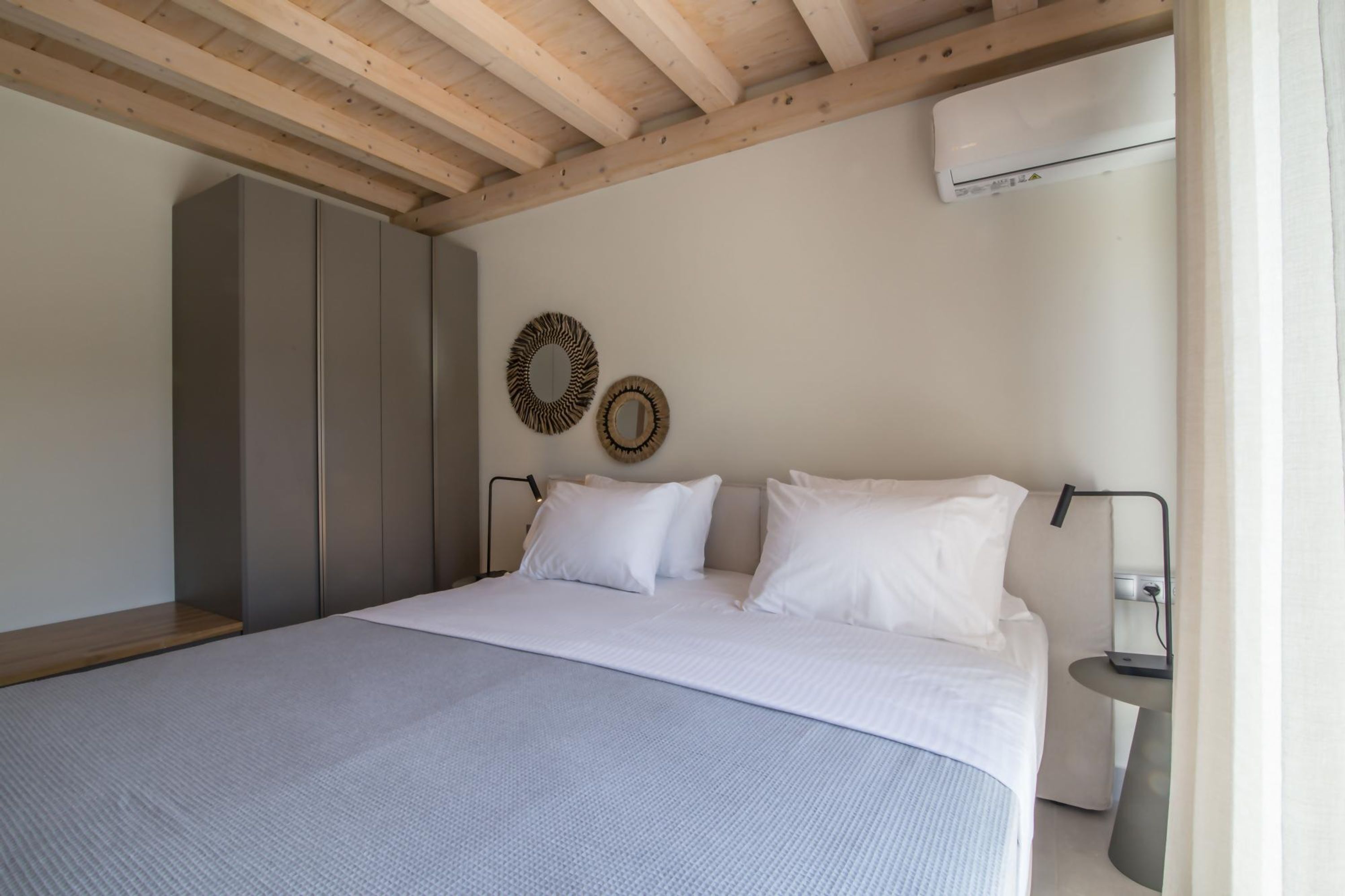 A bedroom with a bed, wardrobe, wall-mounted mirror, and an air conditioning unit.