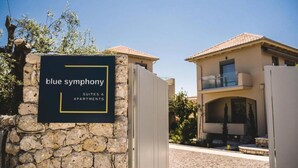 Placa de 'Blue Symphony Suites & Apartments', com uma parede de pedra e um edifício moderno ao fundo.