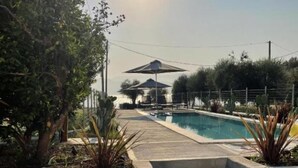 Uma área de piscina com escadas de acesso, rodeada por plantas e guarda-sóis.
