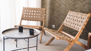 A room with two woven wooden chairs, a round table with a black mug, and a herringbone-patterned wall. - Sea & Pool View Suite (Nikiana)