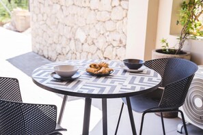 A round table with a geometric patterned tablecloth, two black chairs, a bowl of croissants, and a black bowl on the table. - Sea & Pool View Suite (Nikiana)