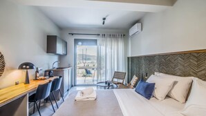 A hotel room with a bed, desk, chairs, and a view of the outdoors. - Sea & Pool View Suite (Nikiana)