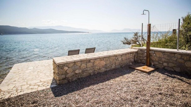 A stone bench by a lake with chairs, a metal fence, and a lamp post. - Sea & Pool View Suite (Nikiana)