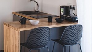 Una cocina compacta con encimera de madera, un lavamanos, dos sillas negras de malla y una cafetera.