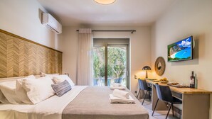 A hotel room with a bed, a desk, a television, and a balcony with a view of greenery. - Garden View  Junior Suite (Nikiana)