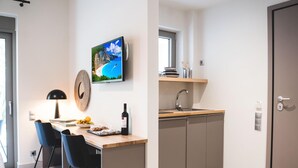 A modern kitchen with a wooden countertop, two black chairs, a wine bottle, and a framed picture of a beach. - Garden View  Junior Suite (Nikiana)