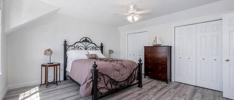Quarto com cama, cómoda, ventoinha no teto e portas brancas.