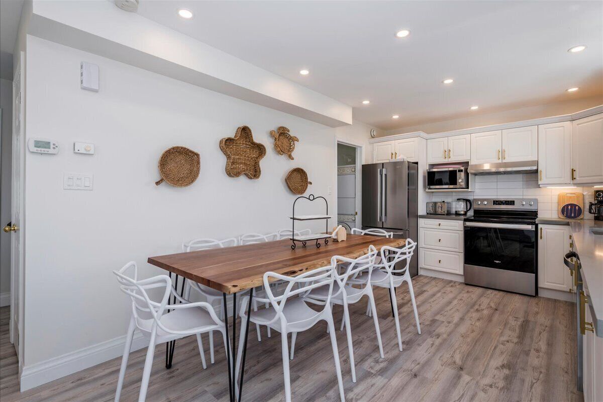 A modern kitchen with white cabinets, stainless steel appliances, and a wooden dining table with white chairs.