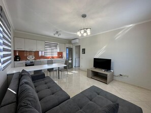 A modern living room with a sectional sofa, a dining area with a white table, and a kitchen with a built-in oven and refrigerator. - Suite 1 - Elpida Luxury Suites (Nydri)