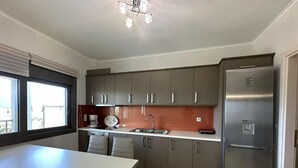 Una cocina moderna con armarios grises, un refrigerador de acero inoxidable, una encimera blanca y un comedor con mesa y sillas.