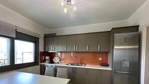 Una cocina moderna con armarios grises, un refrigerador de acero inoxidable, una encimera blanca y un ventanal que proporciona luz natural.