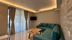 Un salon moderne avec un canapé vert, une table basse en bois et un téléviseur à écran plat fixé au mur.