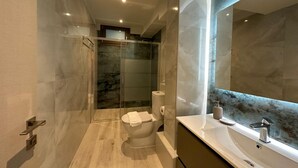 A modern bathroom with a glass shower enclosure, a toilet, and a vanity with a large mirror. - Suite 5 - Elpida Luxury Suites (Nydri)