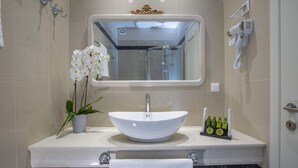 Ein modernes Badezimmer mit einem weißen Waschbecken, einem Spiegel darüber, einem Föhn an der Wand und einer Orchidee im Blumentopf.
