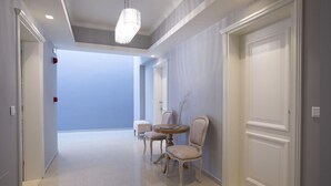 Um corredor com uma mesa redonda e duas cadeiras, um candelabro e uma porta fechada.