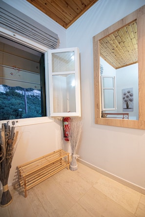 A room with a large window, a mirror, a wooden bench, and a broom. - Caza Levantiera 4 bedroom villa (Kalamitsi)