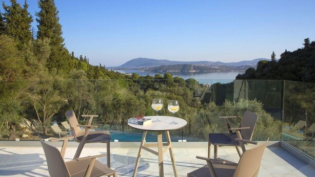 A glass-enclosed outdoor seating area with a table and chairs, overlooking a body of water and hills. - Villa Anticlea Villas Harriet, with sea view! (Ligia)