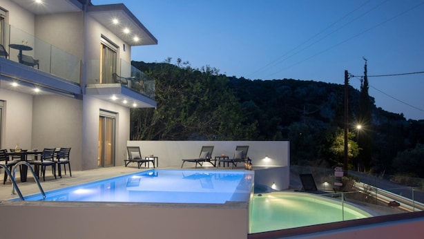 A modern two-story building with a swimming pool, outdoor seating, and a view of a forested hillside. - Aloft Luxury - Villa Lefkia with heated pool (Apolpena)