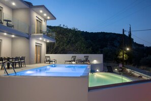 Un moderno edificio de dos pisos con piscina, mobiliario exterior y vistas a una ladera boscosa.